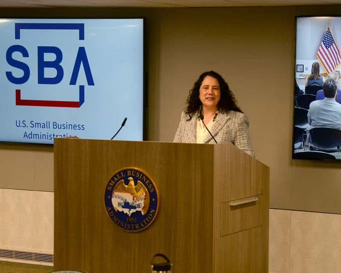 Administrator Guzman speaks at a meeting. A screen with the SBA logo is behind her. 