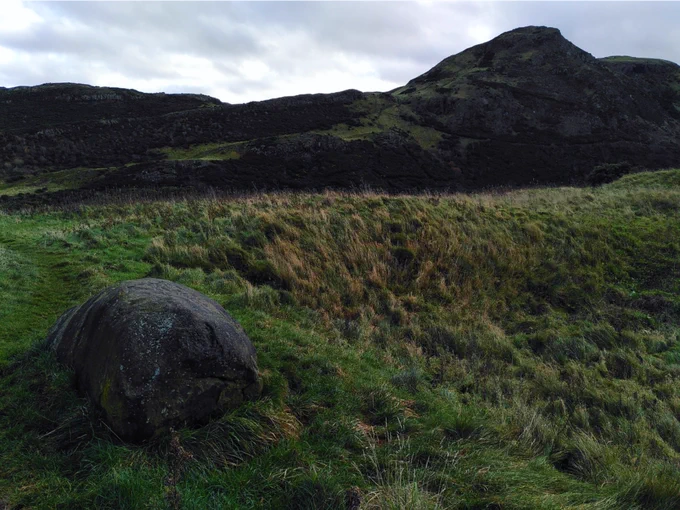 Photo taken in Holyrood park in Edinburgh, showing an erratic in the foreground and volcanic sill in the background.