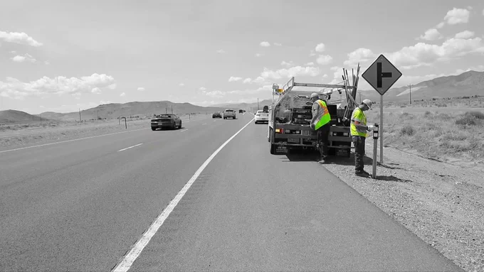 A picture of two NDOT maintenance workers on the side of the highway as vehicles next to them.