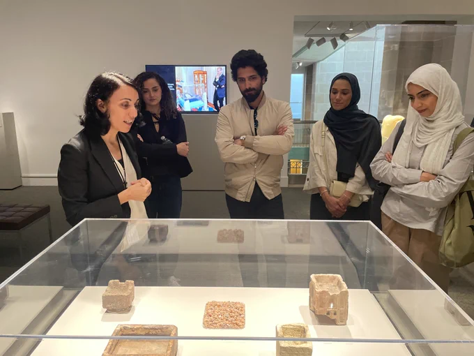 Group of five adults engaged in a discussion at a museum exhibit featuring ancient artifacts in a glass display case.