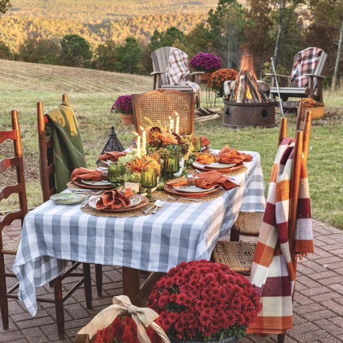 First: An outdoor fall party at sunset near a campfire, including a table set with a gingham tablecloth, taper candles, mums, and cozy blankets. 


