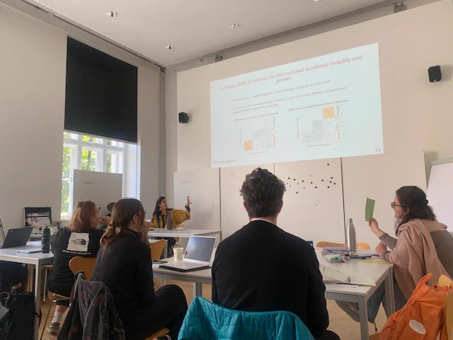 Ana Jaramillo presenting her talk on "The impact of prestige on the visibility of under-represented groups in citation rankings. The intersection of international mobility, nationality and gender".

A class room where the speaker is at the front desk on the left. Her slides are projected on the wall. And participants are in front paying attention to the talk.