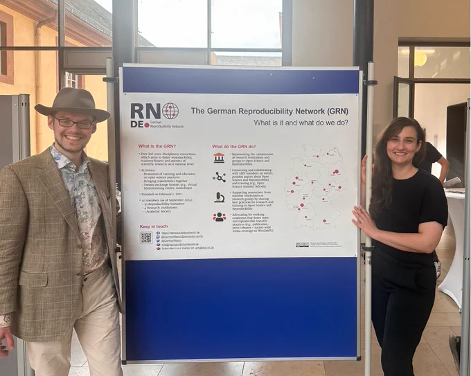 Poster of the German Reproducibility Network, flanked by two GRN representatives. 