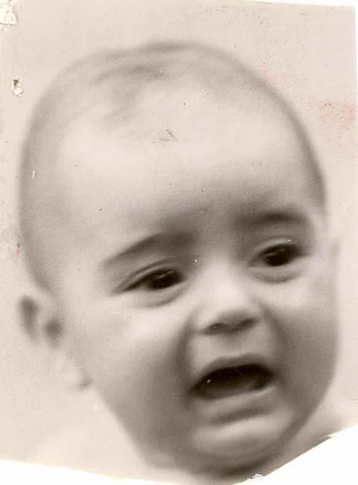 A black-and-white photograph of a baby boy, appearing to be crying or upset. The image is somewhat blurred, but the facial features of the child, including wide eyes and an open mouth, are visible. The baby has a small amount of hair and seems quite young.