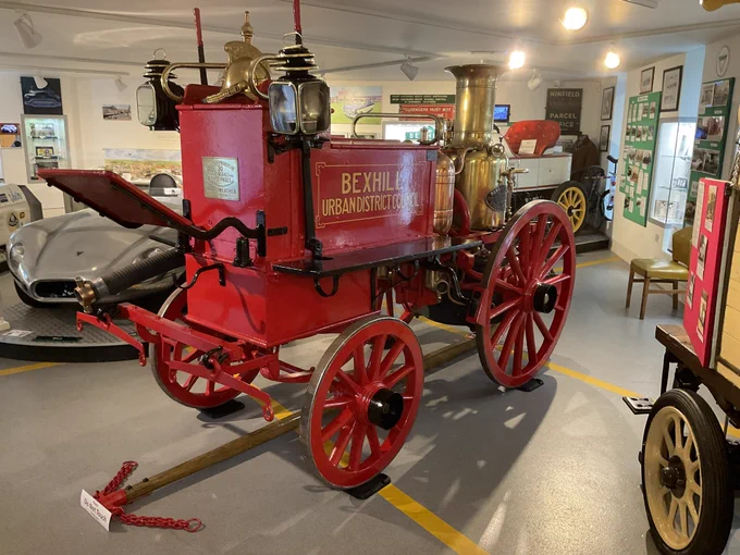 The engine is bright red with Bexhill Urban District Council painted on it in gold. It has shafts at the front where the horse or horses would be. It has a lovely large shiny brass chimney. The two back wheels are larger than the two front wheels.