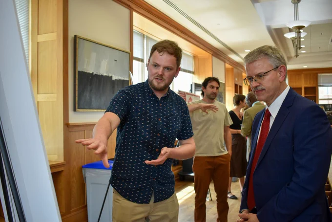 Postdoctoral researcher Alec Nelson (left) gestures to a poster in conversation with Dr. David Pittman (right).