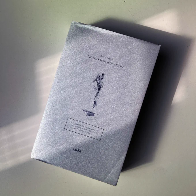 The cover of Notes from isolation on a beige surface. The cover is silver and features the drawing of an abstract figure and the LADA logo. 
