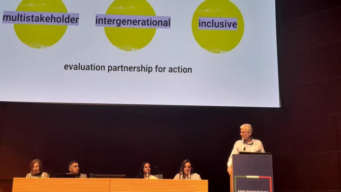 Marco Segone presenting at the EES24 Conference. The text behind him reads, “multistakeholder, intergenerational, inclusive evaluation partnership for action”
