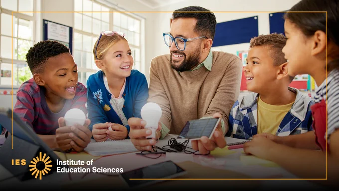A teacher holding a lightbulb smiles with students