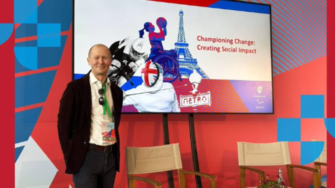 Image of Professor Brett Smith smiling in front of a poster promoting the Paralympics.