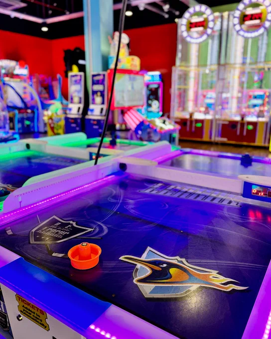Vibrant arcade setting with air hockey tables featuring colorful lighting and background of various arcade games.