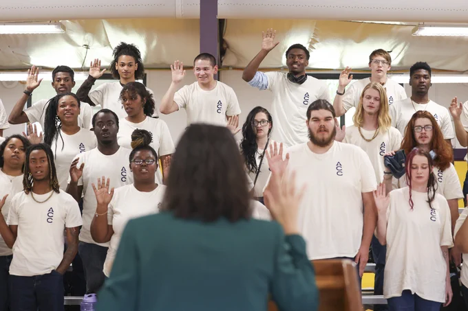 Acting Secretary Julie Su holds up her right hand and faces a group of young people wearing white shirts during a swearing-in ceremony. 