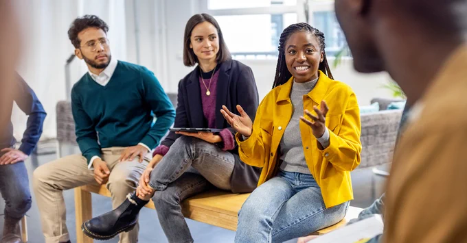 Young woman sharing her view during team building session at startup office. African woman talking with colleagues sitting in circle at a coworking office.
