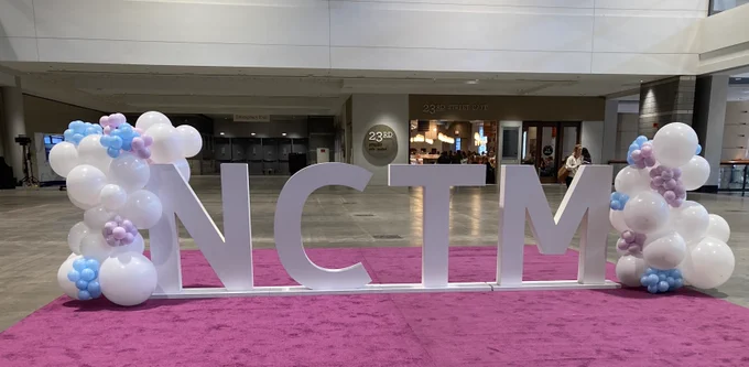 NCTM sign on pink carpet with white, blue, and purple balloons on either side. 
