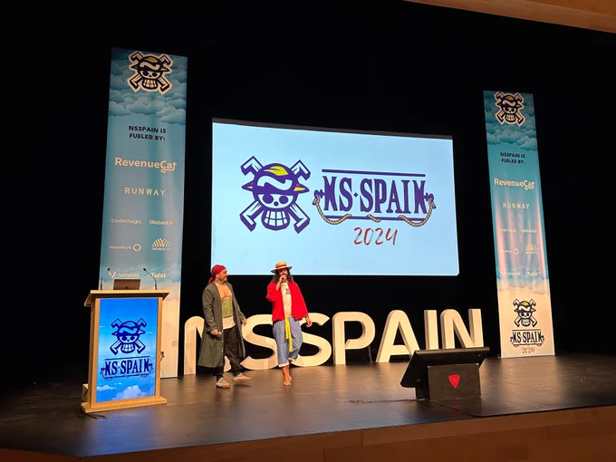 Two men standing on a stage at a conference, holding microphones and talking to attendees