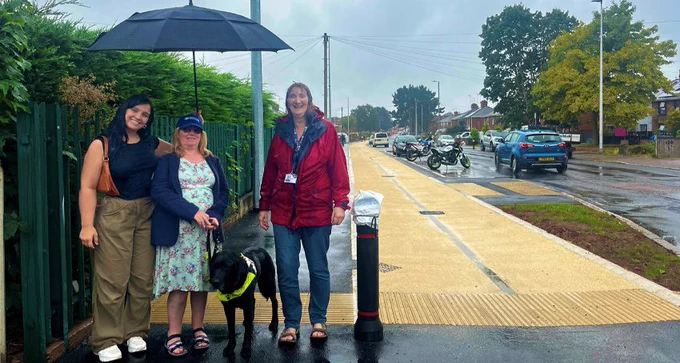 An image of Mandy, Pepsi her Guide dog, India her Support Worker and Liz from Guide Dogs, all standing under an umbrella trying to avoid the the english weather.