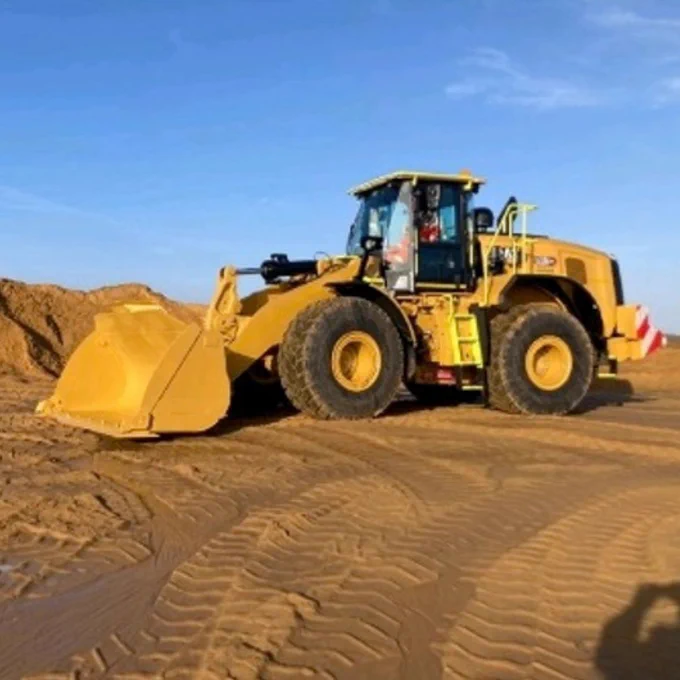 A yellow Caterpillar bulldozer operating on sandy terrain under a clear sky.