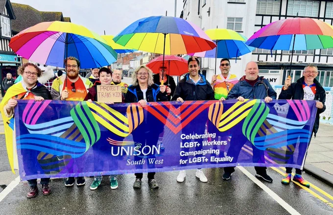 LGBT  SOG members hold UNISON banner at Taunton Pride. Rainbow umbrellas make for a striking, bold and colourful image against a grey, cloudy sky.
