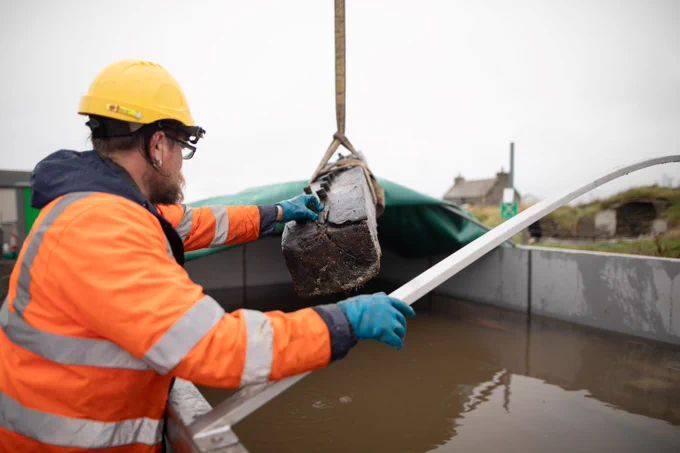 It's a bleak, rainy day in Orkney with a grey sky. Senior marine archaeologist Ben Saunders guides the timbers into the conservation tank.
