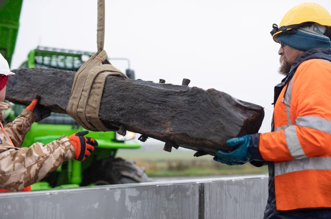 Two men hold either end of the timber as it's lifted into the tank.