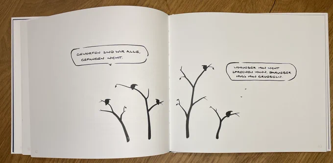 Aufgeschlagene Buchseite mit Cartoons. Vögel sitzen auf Ästen. Einer sagt: geworfen sind wir alle gefangen nicht. Auf der rechten Seite sagt ein Vogel: worüber man nicht sprechen kann, muss man grübeln.