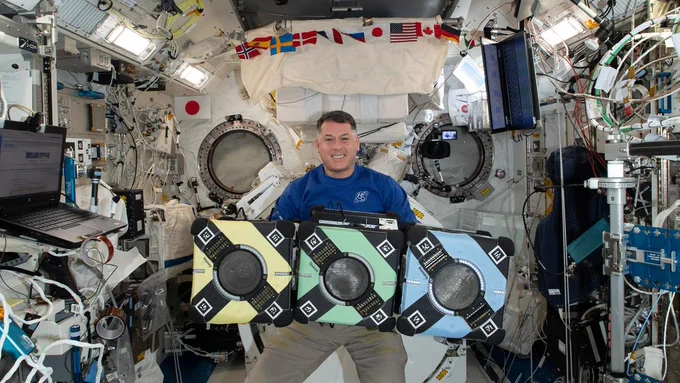 iss065e389375 (9/20/2021) — NASA astronaut Shane Kimbrough poses with the Astrobee robotic free-flyers in support of the Kibo Robot Programming Challenge (Robo-Pro Challenge). The Kibo-RPC, allows students to create programs to control Astrobee, a free-flying robot aboard the International Space Station (ISS).