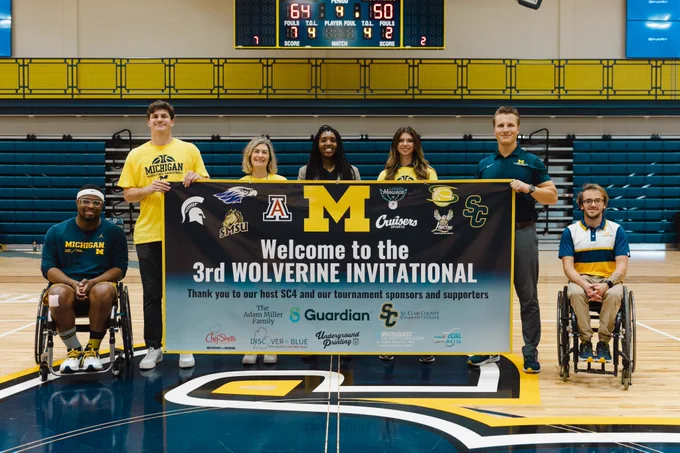 Individuals from the university of michigan adaptive sports program standing with a sign for the post game awards ceremony 