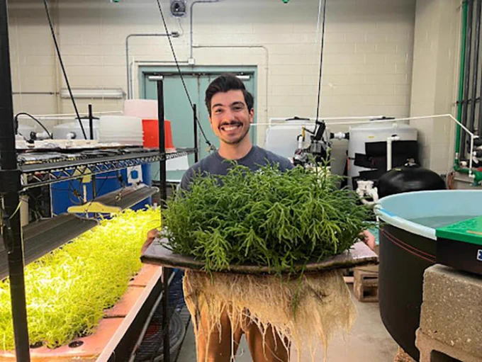 Scientist stands in a wetlab holding a tray of sea beans.