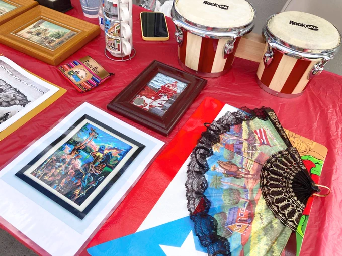 Table with various framed pictures, a hand fan, small objects including a smartphone, ceramic mugs, and two hand drums labeled “RockJam."