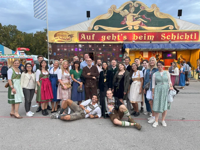 A group of people in traditional Bavarian outfits posing in front of the Schichtl theatre at Oktoberfest.