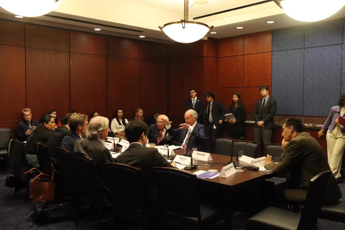 Senator Markey speaks from a table in a room with wooden walls. He is seated next to global climate leaders.