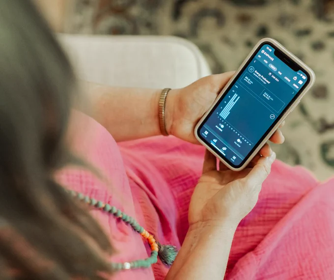 Person sitting and holding a smartphone looking at how much energy her solar panels are generating.