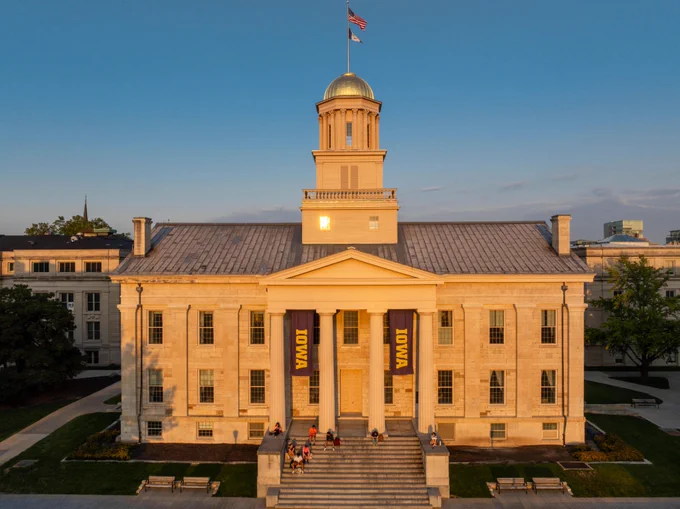 Photo of the Old Capitol Building with students sitting on the steps as the sun sets.