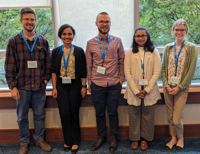 Five attendees of ASBMB's transcriptional regulation meeting smile while wearing conference badges and standing in front of a large window. Trees are outside. 