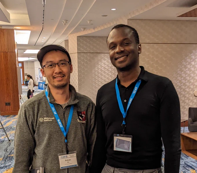 Two attendees of the ASBMB's meeting on transcriptional regulation smile for a photo. One attendee is wearing a baseball cap and grey quarter zip pullover, the other attendee is wearing a black, long-sleeve polo shirt.