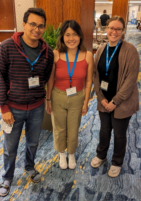 Three attendees of ASBMB's meeting on transcriptional regulation smile for a photo. There is a plant and wood column behind them. 