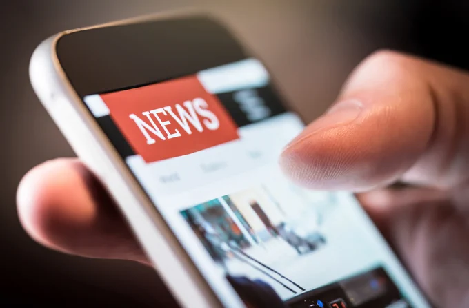 A photo of a hand scrolling through a newsfeed on their phone. 