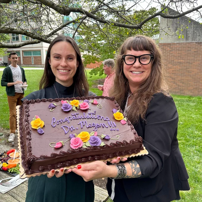 Dr. Megan Barkdull and Dr. Corrie Moreau holding a cake to celebrate Megan successfully defending her Ph.D.