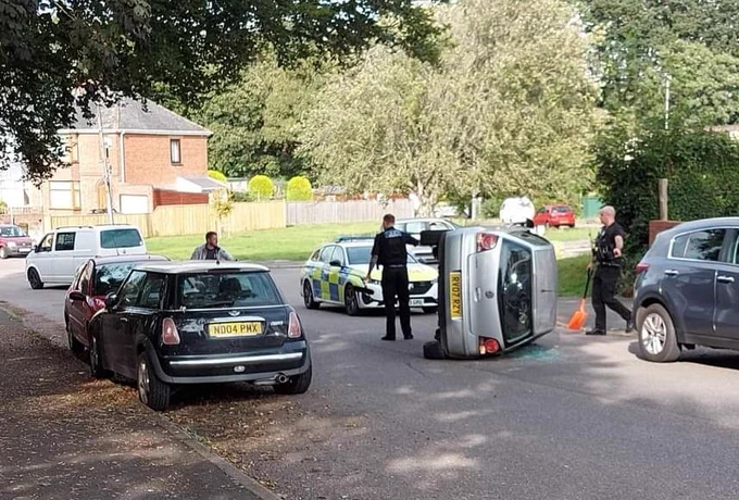 Car lies on its side on residential street (where a bollards reducing rat running had recently been removed). Police are in attendance at the scene. 