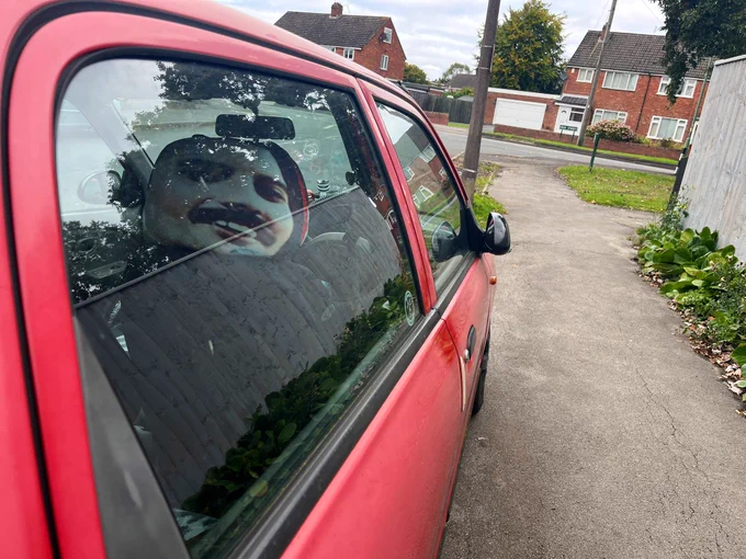 A red car with. Freddie Mercury headrest on the back of the front seat