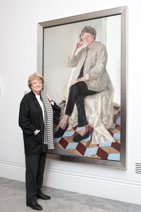 [IMAGE] The actor Dame Maggie Smith stands in front of her painted portrait. She is wearing a dark suit and white top.