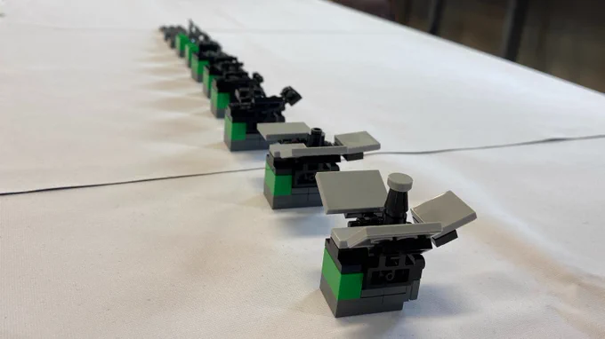 A mini Lego construction of the A-DOT space telescope is placed on a table in the foreground, with elements missing the further back you look into the image. This demonstrates the building process of the Lego model. 