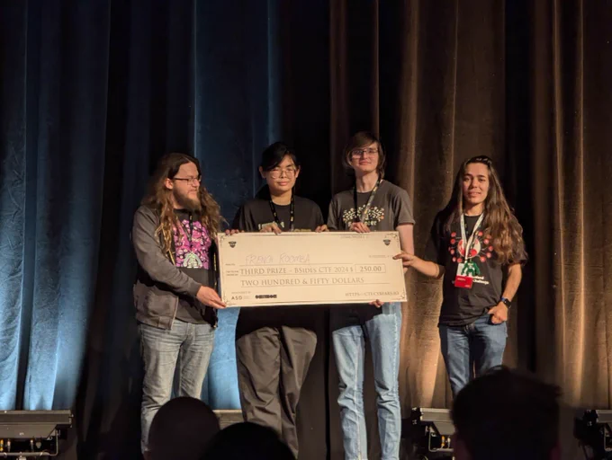 Photo of 4 members from CTF team FrenchRoomba on stage holding up a novelty check.