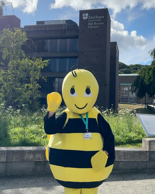 Billy Bee, the library mascot, waving at the camera. They are standing outside of Bill Bryson Library.