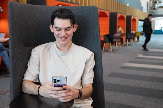 Photo of a student using a mobile phone while sitting in one of BCU's Curzon Library study spaces