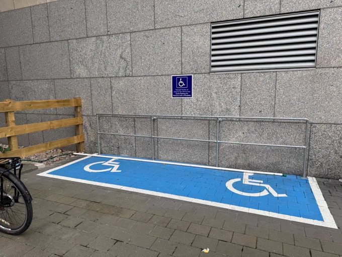 Blue cycle parking with international wheelchair symbol. Railing at back to lock bike to. 