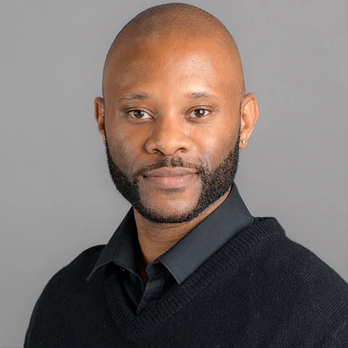 A photograph of Kevin Brazant in a black shirt and a V neck jumper