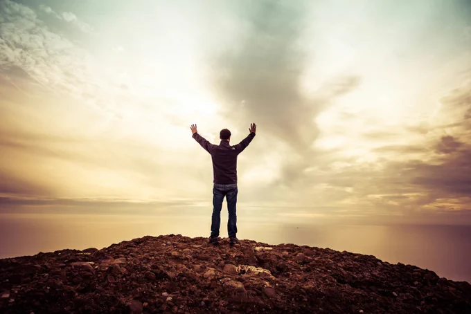 Man standing with arms outstretched on top of a hill. Photo by Guillaume de Germain on Unsplash
