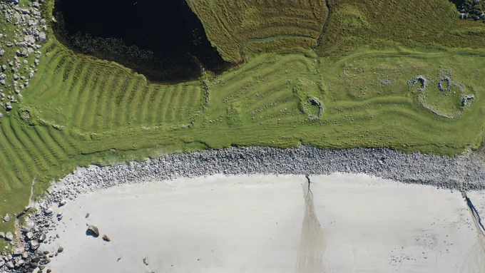 Layers of history are revealed in this bird's eye view of Traigh Daoidhn at Crabhadail in North Harris. A shieling (seasonal dwelling) is tucked into feannagan (cultivation ridges) which curve around the sites of still older houses. A later sheepfold (but still old!) shows up in fresh white stone. Old Norse and Gaelic placenames of every natural feature in this landscape also tell the story of its long history.