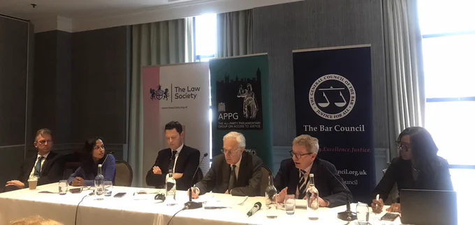 Panel table with six people, four white men, one South Asian woman and one Black woman